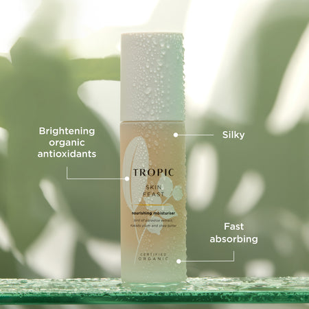 This image features a bottle of Skin Feast, a nourishing moisturiser. Key attributes are highlighted:
Brightening organic antioxidants for skin protection and radiance.
Silky texture for a luxurious application.
Fast absorbing formula to deliver instant hydration.
The product contains ingredients like bird of paradise extract, Kakadu plum extract and shea butter.  The dewy aesthetic emphasises its hydrating and refreshing properties.